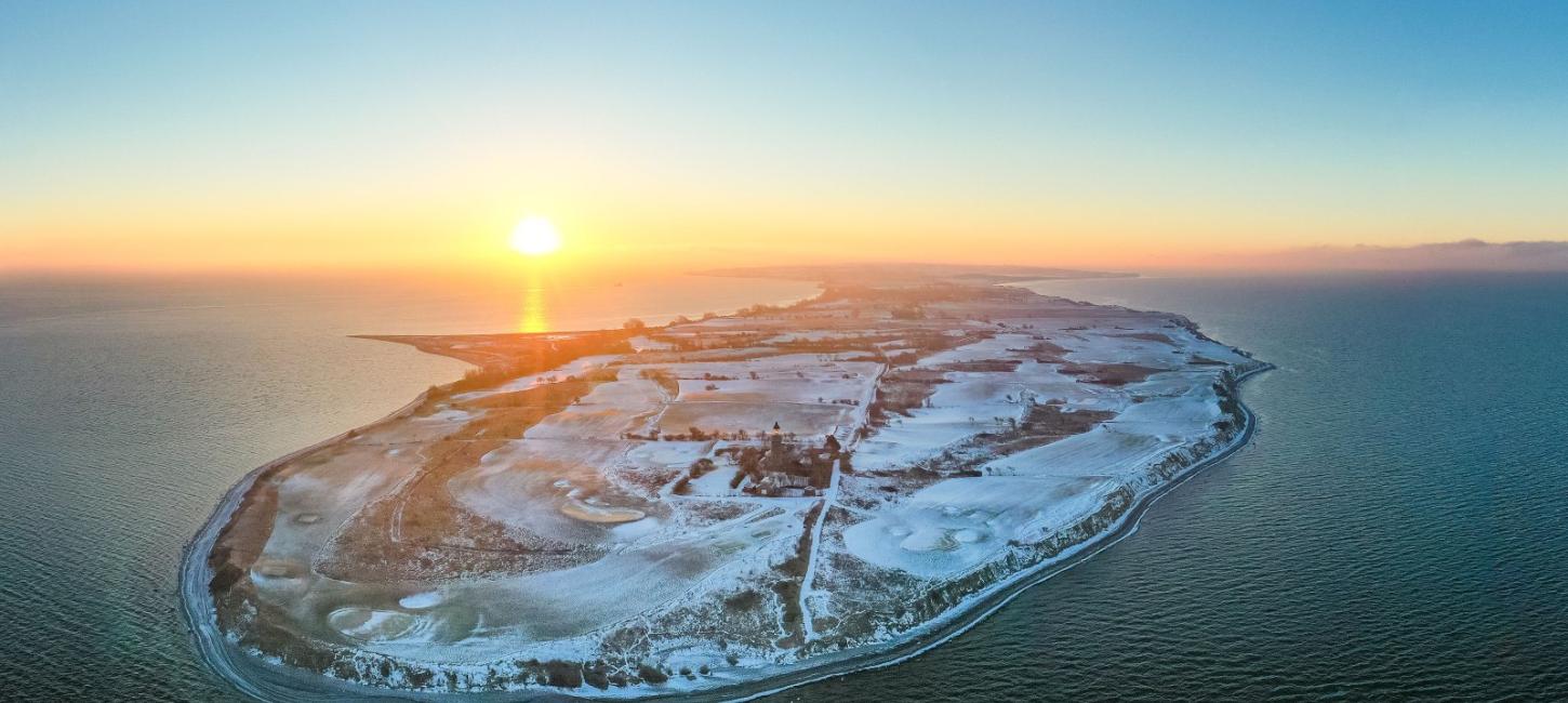 Luftfoto af Vestærø, fyr og golfbane med sne og solnedgang