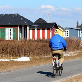 Mand cykler langs badehuse og sne ved Vesterstrand om vinteren